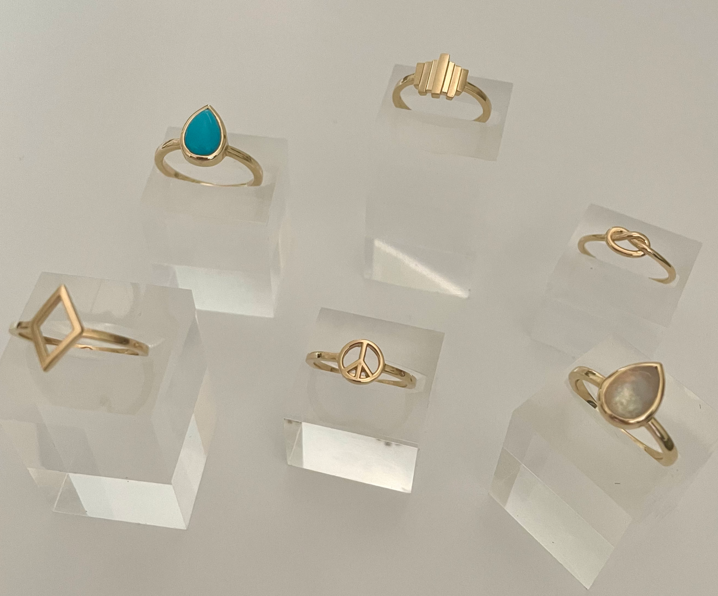 Gold rings displayed on clear stands against a light gray background