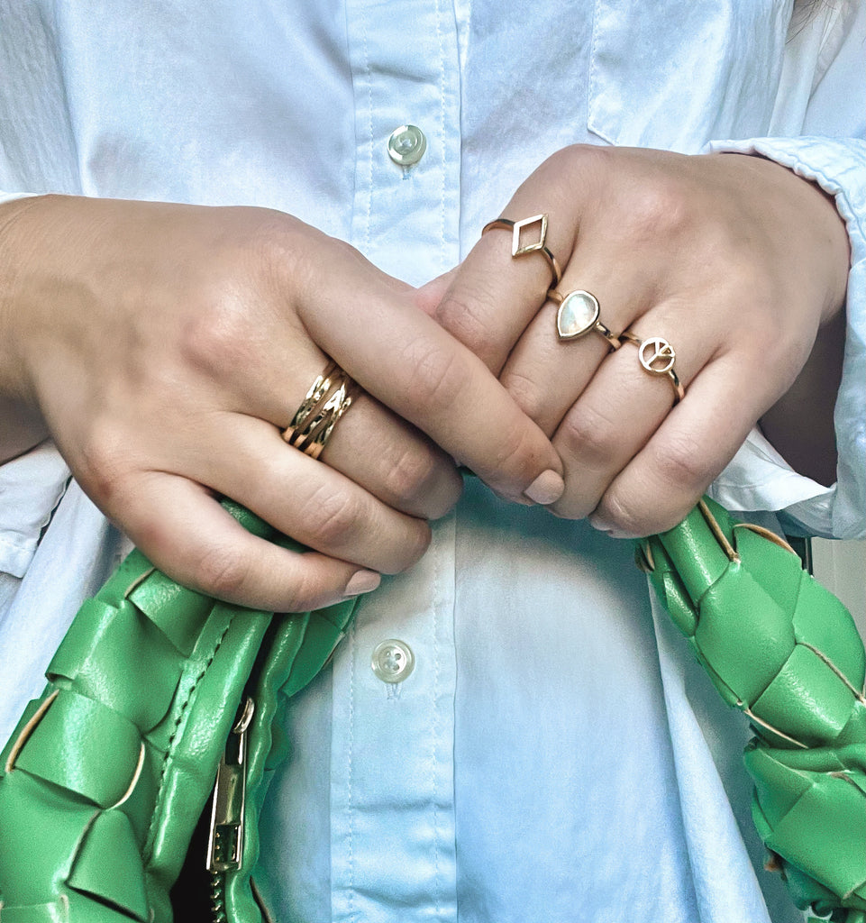 white button down and a green leather woven bag paired with the solid 14k gold orbit ring, diamond outline ring, rainbow moonstone gemstone ring, and peace sign ring